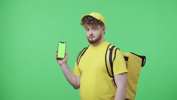 Yeşil ekranlı telefonu tutan genç adamların portresi, başparmaklarını gösteriyor. Sarı kurye üniformalı, yeşil ekranda duran termo çantalı kızıl saçlı erkek. Kapatın. Yavaş çekim hazır 59.97fps. — Stok video