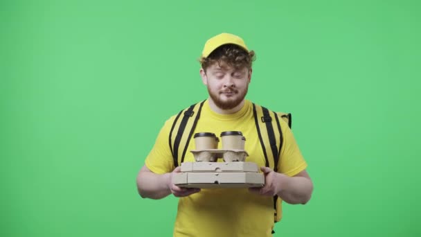 Portret młodych mężczyzn trzymających kawę i pizzę, cieszących się aromatem, rozciąga je w kamerę. Rudowłosy mężczyzna w żółtym mundurze kurierskim, pozujący na zielonym ekranie. Zamknij drzwi. Wolny ruch gotowy 59.97fps — Wideo stockowe