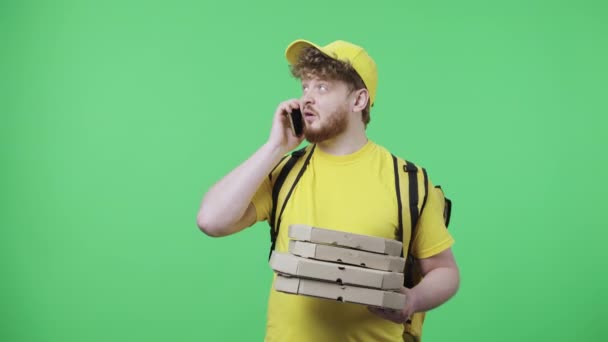 Portrait de jeunes hommes parlant au téléphone laisse tomber des boîtes à pizza et est très contrarié. Rousse mâle en uniforme de messagerie livraison jaune avec sac thermique posant sur écran vert. Ferme là. Ralenti prêt 59.97fps — Video