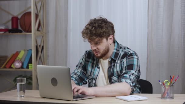 Junger Mann im karierten Hemd tippt auf die Laptop-Tastatur, schließt sie wütend, öffnet sie dann und tippt weiter. Rothaarige Männchen mit Bart sitzen im Home Office. Aus nächster Nähe. Zeitlupe bereit 59.97fps — Stockvideo