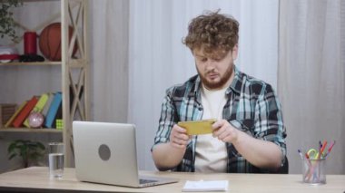 Kareli gömlekli genç adam akıllı telefonuyla oyun oynuyor ve zaferle seviniyor. Kızıl saçlı, sakallı bir erkek merkez ofiste dizüstü bilgisayarın yanında oturuyor. Kapatın. Yavaş çekim hazır 59.97fps.