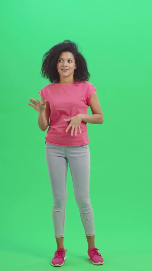 Porträtt av unga kvinnliga afroamerikaner rapporterar och berättar mycket intressant information. Svart kvinna poserar på grön skärm. Slow motion klar 59,97fps. fp. Vertikal video. Full längd. — Stockvideo