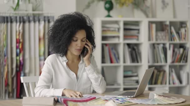 Portrait of young African American woman looking through color palette and samples of fabrics and discussing design of project by phone. Close up. Slow motion ready 59.97fps. — Stock Video