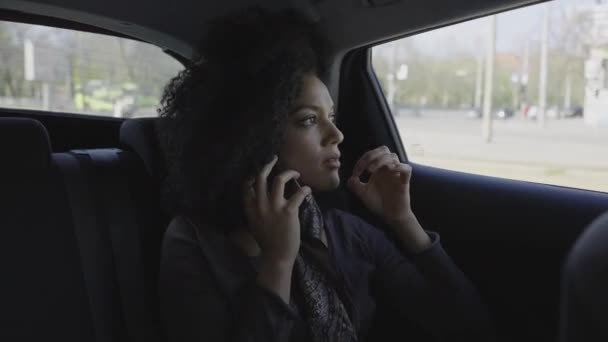 Portrait de la jeune femme afro-américaine élégante parlant sur smartphone. Une femme de race mixte dans une voiture sur le siège arrière. Ferme là. Ralenti prêt 59.97fps. — Video