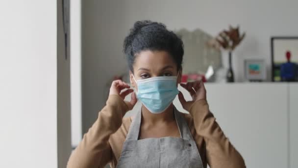 En vacker afroamerikansk kvinna som häller ut en medicinsk mask och suckar av med lättnad. Ung kvinnlig blandras poserar mot bakgrund av ett ljust rum. Närbild. Långsamma rörelser. — Stockvideo