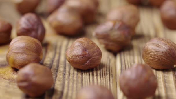 Avelãs secas que se encontram em uma superfície de mesa de madeira texturizada. Os grãos castanhos descascados caem sobre a mesa. Fundo alimentar saudável orgânico. Fecha. Movimento lento. — Vídeo de Stock