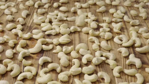 Anacardo crudo acostado sobre una superficie de mesa de madera texturizada. Los granos blancos pelados caen sobre la mesa. Fondo de alimentos orgánicos saludables. De cerca. Movimiento lento. — Vídeos de Stock