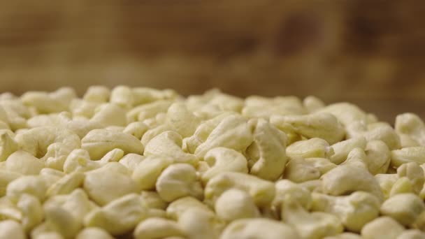 Rauw draaiend cashewtje. Witte pitten vallen op een stapel geschilde noten. Biologische gezonde voedselachtergrond. Sluit maar af. Langzame beweging. — Stockvideo
