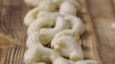 Ahşap desenli masa yüzeyinde bir sırada duran taze çiğ kaju. Bütün fındık çekirdekleri masaya yakın bir şekilde serilmiş. Organik sağlıklı gıda geçmişi. Yavaş çekim hazır 59.94fps.