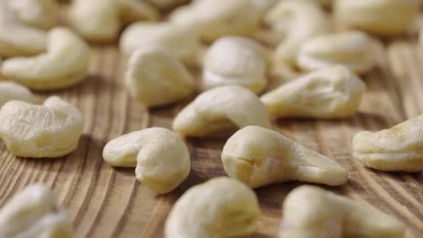 Foto deslizante de nueces frescas de anacardo crudo que se encuentran sobre una superficie de mesa de madera texturizada. Los núcleos enteros se encuentran dispersos sobre la mesa. Fondo de alimentos orgánicos saludables. Cámara lenta lista 59.94fps. — Vídeo de stock