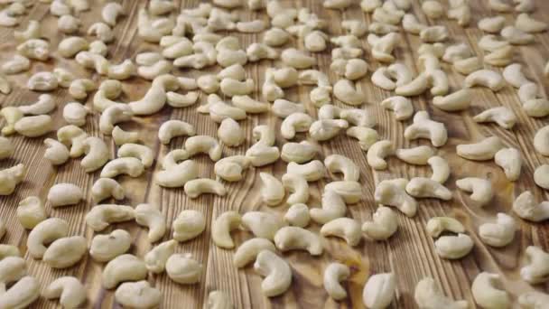 Glidbild av färska råa cashewnötter som ligger på en strukturerad träbordsyta. Närbild hela kärnor är utspridda på bordet. Ekologisk hälsosam mat bakgrund. Slow motion klar 59,94fps. — Stockvideo