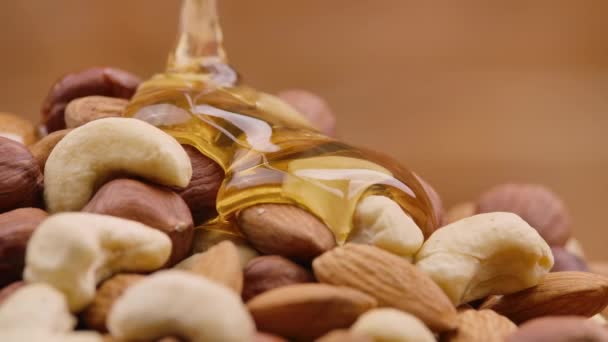 Ein Rinnsal goldenen Honigs fließt in Zeitlupe einen Haufen Nüsse hinunter. Honig tropft und umhüllt die Mischung aus Mandeln, Cashewnüssen und Haselnüssen. Detailaufnahme von Nüssen in süßem Sirup. — Stockvideo