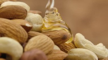 Altın bal damlaları yavaş çekimde bir yığın fındığa akar. Badem, fındık ve fındık karışımını bal damlatır ve sarar. Tatlı şuruplu fındıkların detaylı görüntüsünü kapat..