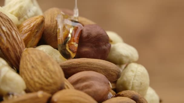 Trickle av gyllene honung flyter ner en hög nötter i slow motion. Honung droppar och omsluter blandningen av mandel, cashewnötter och hasselnötter. Närbild detaljerad bild av nötter i söt sirap. — Stockvideo