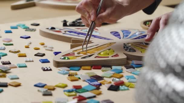 Mani maschili creano mosaici con pinzette e piccoli pezzi luminosi di vetro e ceramica. Maestro artigiano rendendo modello farfalla colorata in un laboratorio creativo. Chiudete. Movimento lento pronto 59.94fps. — Video Stock