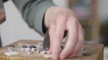 Erkek eller özel bir çekiçle mozaik fayansları ikiye böler. Mozaik desen oluşturmak için taş malzemelerin hazırlanması. Yaratıcı bir atölyede el yapımı. Kapatın. Yavaş çekim.