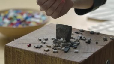 Mozaik fayansları ayırmak için çekiç yakın çekim. Erkek eller küçük mozaik taş parçalarını metal bir aletin üzerine döküyorlar. Yaratıcı bir atölyede el yapımı. Yavaş çekim.