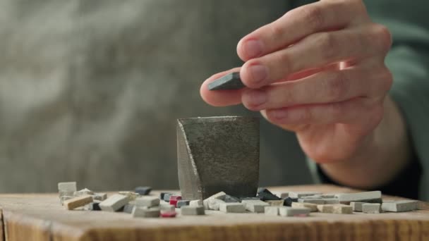 Mannelijke handen breken de mozaïektegels in tweeën met een speciale hamer. Voorbereiding van stenen materiaal voor het leggen van een mozaïek patroon. Handgemaakt in een creatieve werkplaats. Sluit maar af. Langzame beweging. — Stockvideo