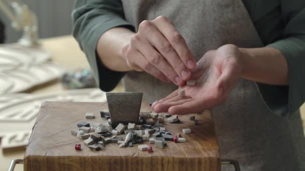 Mannelijke handen verzamelen gebroken stukken steen om een mozaïek patroon te leggen. Voorbereiding van stenen materiaal voor het leggen van een mozaïek patroon. Handgemaakt in een creatieve werkplaats. Sluit maar af. Langzame beweging. — Stockvideo