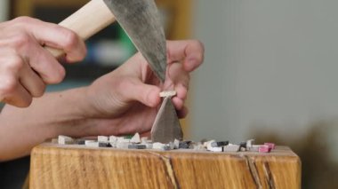 Erkek eller özel bir çekiçle mozaik fayansları ikiye böler. Mozaik desen oluşturmak için taş malzemelerin hazırlanması. Yaratıcı bir atölyede el yapımı. Kapatın. Yavaş çekim.