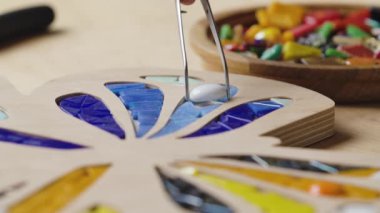 Erkek eller cımbızla, parlak cam ve seramiklerle mozaikler oluştururlar. Usta zanaatkar yaratıcı bir atölyede renkli kelebek desenleri yapıyor. Kapatın. Yavaş çekim.
