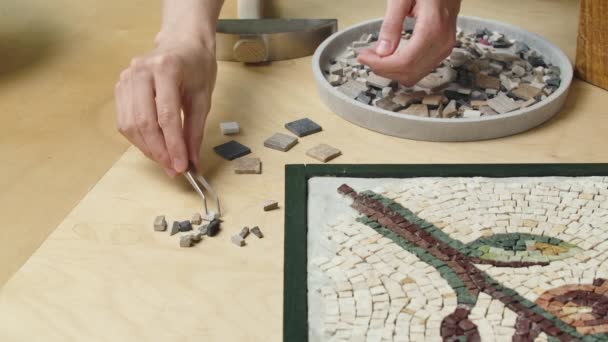 Mannelijke handen maken mozaïeken bloemenpatroon met behulp van pincet en kleine stukjes graniet steen. Master handwerk maken in een creatieve werkplaats. Interessante hobby, kunst, kunstwerk. Sluit maar af. Langzame beweging. — Stockvideo