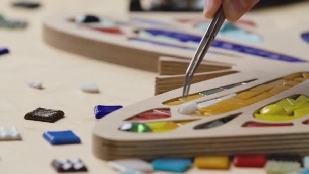 Las manos masculinas crean mosaicos con pinzas y pequeñas piezas brillantes de vidrio y cerámica. Artesano maestro haciendo patrón de mariposa de colores en un taller creativo. De cerca. Movimiento lento. — Vídeos de Stock