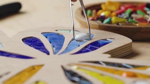 Manliga händer skapar mosaiker med pincett och ljusa små bitar av glas och keramik. Master hantverkare gör färgglada fjäril mönster i en kreativ verkstad. Närbild. Långsamma rörelser. — Stockvideo