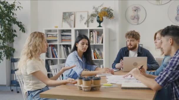 Un gruppo di giovani uomini e donne siede a tavola in un ufficio moderno e discute di questioni di lavoro nel corso di una riunione negoziale. Dipendenti qualificati che sviluppano una strategia di startup marketing. Rallentatore. — Video Stock