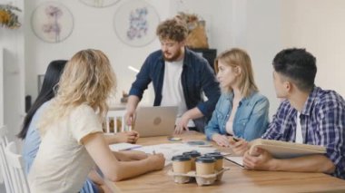 Bir grup genç erkek ve kadın modern ofiste masada oturuyorlar ve müzakere toplantısında iş meselelerini tartışıyorlar. Nitelikli çalışanlar başlangıç pazarlama stratejisi geliştiriyor. Yavaş çekim.