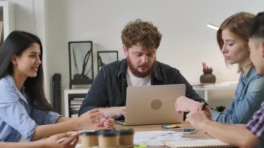 Modern ofiste masada oturan ve müzakere toplantısında iş konularını tartışan bir grup genç erkek ve kadın. Nitelikli çalışanlar başlangıç pazarlama stratejisi geliştiriyor. Ağır çekim. Kapat..