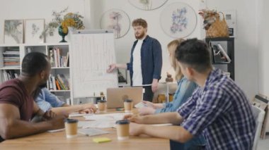 Genç erkek takım lideri kurulun yanında duruyor ve yeni bir başlangıç projesi sunuyor. Karışık ırk meslektaşları müzakere toplantısında iş meselelerini tartışıyor. Yavaş çekim.