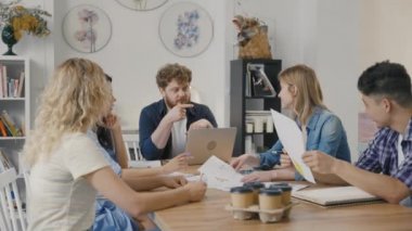 Bir grup genç erkek ve kadın modern ofiste masada oturuyorlar ve müzakere toplantısında iş meselelerini tartışıyorlar. Nitelikli çalışanlar başlangıç pazarlama stratejisi geliştiriyor. Yavaş çekim.