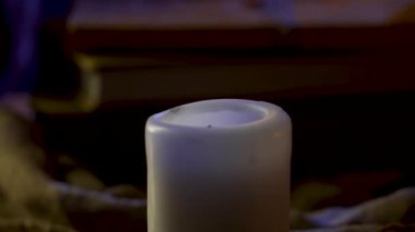 Bir yığın kitabın bulanık arka planına karşı sönmüş beyaz bir mum karanlık bir odada duruyor. Cadılar Bayramı. Ağır çekim. Kapat..