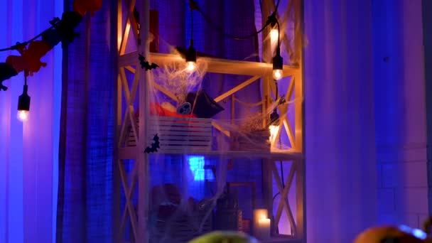 Chambre fumée décorée pour Halloween. Le mouvement de la caméra d'un rack, avec des bougies allumées et une guirlande, à une table sur laquelle repose une citrouille avec un visage effrayant peint. Au ralenti. Gros plan. — Video