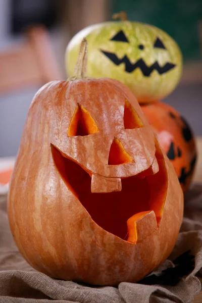 Citrouille Jack o Lanterne avec sourire sculpté. Gros plan d'une citrouille avec un sourire sculpté sur la table, et au dos il y a deux autres citrouilles avec des visages effrayants peints. Plan vertical. — Photo