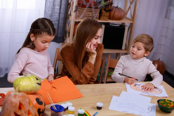 Children prepare Halloween decorations, paint and carve. A loving mother next to them at the table helps them with this. Happy family party at home. Top view. Close up. — Stock Photo, Image