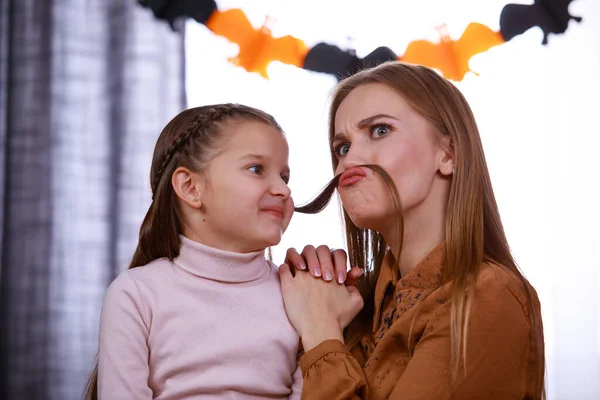 Mamãe está sentada em uma sala decorada para o Halloween e brincando com sua filha. Uma mulher faz-se um bigode de um fio de cabelo de suas filhas. Fechar. — Fotografia de Stock