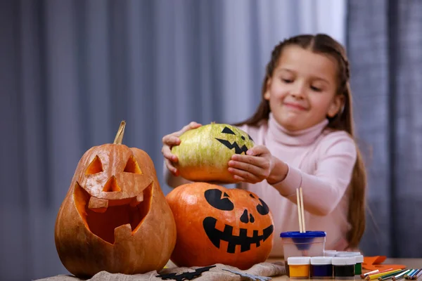 A preparar-se para o Halloween. Na mesa estão abóboras com um rosto pintado e esculpido terrível, a menina estabelece outro. Dia das Bruxas. Fechar. — Fotografia de Stock