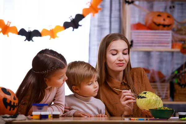 Mamãe desenha um focinho assustador em uma abóbora de Halloween para esculpir uma lanterna e mostra para as crianças. Família feliz em casa se preparando para o Halloween, fazendo decorações. Férias em família. Fechar. — Fotografia de Stock