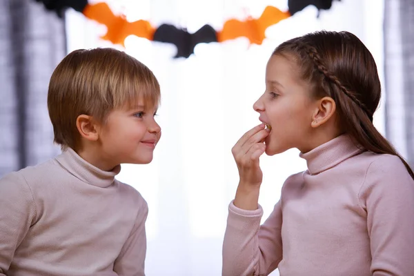 Menino e menina em um quarto decorado para o Halloween. A irmã come uma guloseima na frente de seu irmão, e o menino sorri para ela. Feliz festa de família em casa. Fechar. — Fotografia de Stock