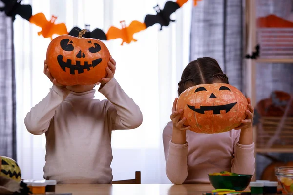 Duas crianças, um menino e uma menina, criaram abóboras na frente deles e mostram seus rostos assustadores pintados. As crianças adoram o Halloween. Fechar. — Fotografia de Stock