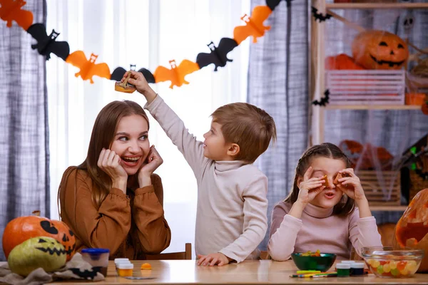 Szczęśliwa rodzina przygotowuje się do Halloween w domu. Mama, córka i syn siedzą przy stole i bawią się rzeźbionymi nożycami do dyń. Szczęśliwej rodzinnej imprezy w domu. Zamknij się.. — Zdjęcie stockowe