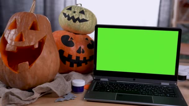 Odadaki masada üzerinde krom anahtar olan yeşil ekran maketi olan modern bir laptop var. Dizüstü bilgisayarın yanında korkunç yüzler ve guaj ile kesilmiş balkabakları var. Balkabaklarını yakınlaştır. Ağır çekim. Kapat.. — Stok video