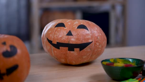 Citrouilles d'Halloween avec des visages effrayants peints décor intérieur. Deux citrouilles et friandises sont sur la table dans la pièce. Automne amusant et décoration effrayante. Halloween. Zoom arrière. Au ralenti. Gros plan. — Video