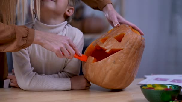 A mãe mostra ao filho como fazer uma cara de Lanterna Jack de Halloween na grande abóbora laranja. Feche de uma mão de mulher que esculpe uma cara terrível em uma abóbora. Movimento lento. — Vídeo de Stock