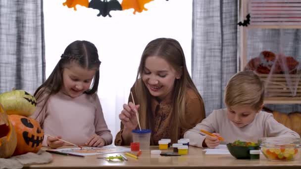 Šťastná běloška a její dvě děti, dcera a syn, sedí u stolu, povídají si a kreslí dýně. Dekorace domu na Halloween. Zpomal. Zavřít. — Stock video