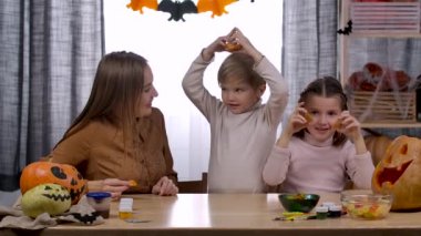 Mutlu aile evde Cadılar Bayramı için hazırlanıyor. Anne, kız ve oğul oyulmuş balkabağı keskisiyle kendilerini eğlendiriyorlar. Onları boynuzları, gözleri, burnu ve şapkasıyla temsil ediyorlar. Ağır çekim. Kapat..