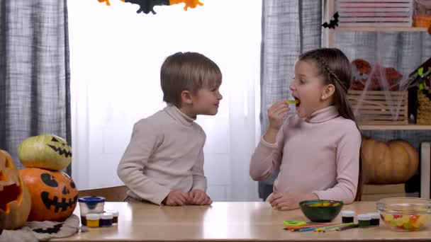 La hermana se burla de su hermano con un gusano de gelatina y se lo come ella misma, a lo que el niño comienza a reír y golpear sus puños en la mesa. Feliz fiesta familiar en casa. En cámara lenta. De cerca.. — Vídeo de stock