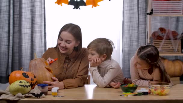 Mom, daughter and son carve Jacks flashlight from a pumpkin. Mom cuts a piece of vegetable and everyone takes turns inhaling the aroma of the juicy pumpkin. Slow motion. Close up. — Stock Video